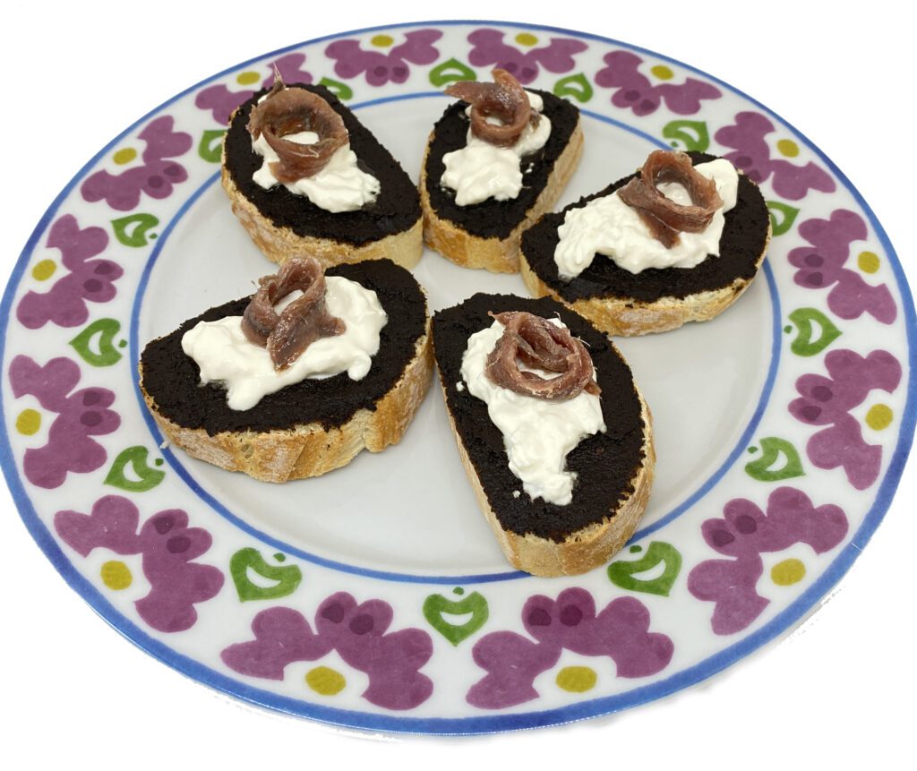 Crostini con aglio nero, burrata e acciughe.
