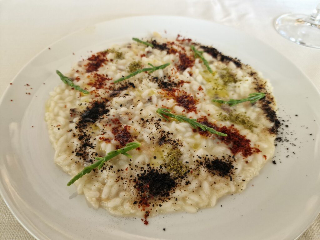 Risotto camouflage alle vongole con polvere di aglio nero, peperone crusco e salicornia croccante.
