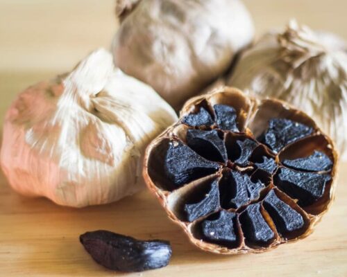 Bulbo di aglio nero aperto con spicchi neri e bulbi interi di aglio.